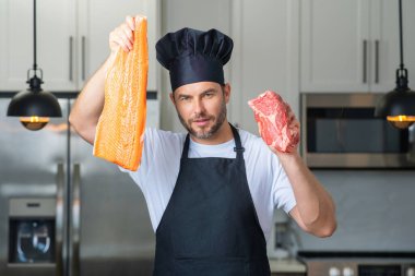 Bin yıllık İspanyol şef üniformalı adam mutfakta balık ve et, somon ve biftek tutuyor. Balık ve et pişiriyorum. Balık ve etli restoran menüsü. Yemek pişirme, balık ve et reklamı konsepti