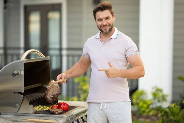 バーベキューマスター バーベキュー用のエプロンを着た中年のヒスパニック系男性 ローストやグリル料理 男は調理器具バーベキューを保持します 肉を屋外で焙煎する バーベキューとグリル 裏庭で肉を調理 — ストック写真