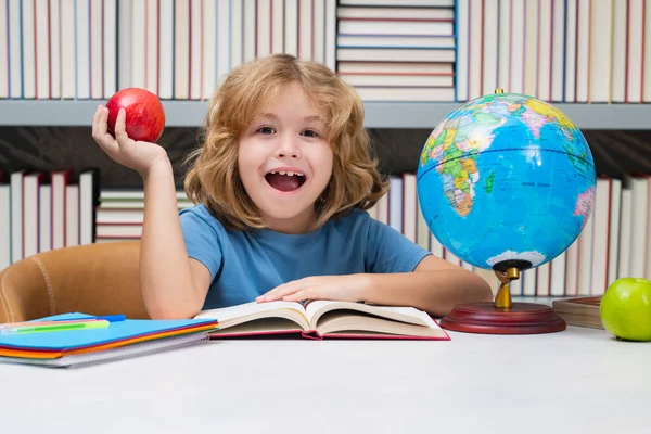 興奮した生徒だ 図書館で本とリンゴを持つ学校の少年 本を持って7 8歳の子供は学校に戻ります 小学生 — ストック写真