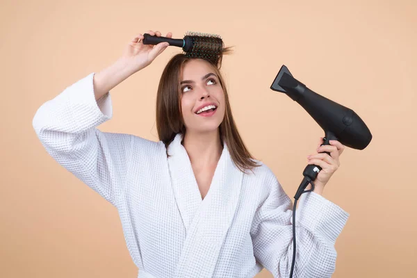 가운을 여자가 머리를 헤어드라이어로 머리카락을 말린다 머리를 빗으로 솔질하는 모델의 — 스톡 사진