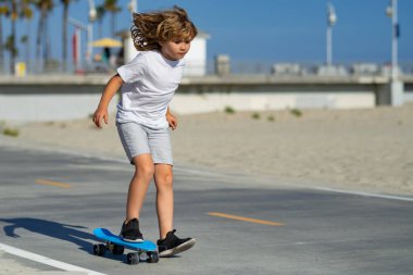 Kid boy riding skateboard in the road. Kid practicing skateboard. Children learn to ride skateboard in a park on sunny summer day. Active leisure and outdoor sport for child