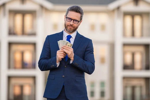 Portrait business man holding cash dollar bills front of house outdoor. Big luck. Dollar cash money concept. Rejoices to win cash. Man hold cash money. Financial luck and success. Manager or realtor