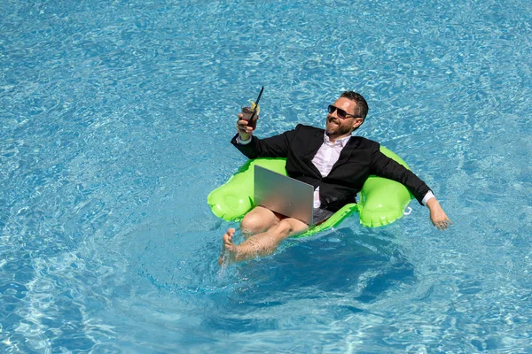 stock image Funny business man in a business suit floating in the water in the pool. Remote work. Crazy freelancer. Business and summer. Business man drink summer cocktail and using laptop in pool