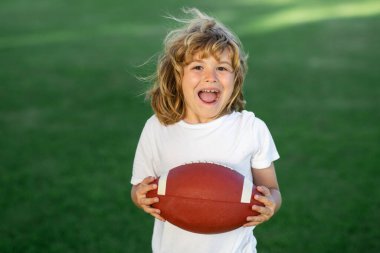 Sporcu çocuk. Çocuk yeşil çim parkında eğleniyor ve Amerikan futbolu oynuyor.