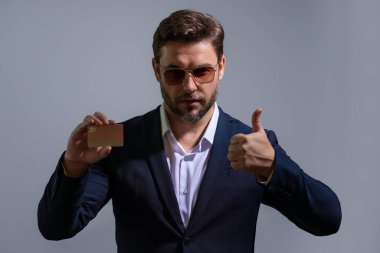 Elinde kredi kartı tutan yakışıklı bir adam. Gri stüdyo geçmişinde kredi kartı olan orta yaşlı bir adam. Kredi kartı konsepti. Takım elbiseli bir işadamı kredi kartıyla ödeme yapıyor.