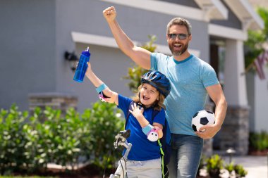 Sportif aile. Kazanan jest ile heyecanlı baba ve oğul. Baba oğlunun bisiklete binmesine yardım ediyor. Kasklı küçük çocuk babasıyla bisiklet sürmeyi öğreniyor. Babalar Günü