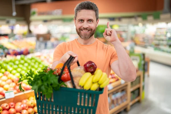 Man with fruits and vegetables at grocery store. Healthy food for mens health. Man with shopping cart full of fresh vegetables. Man at grocery store or supermarket