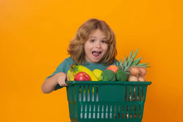 Grocery shop. Excited kid at vegetable supermarket. Child with shopping basket. Child choosing food in store or grocery store