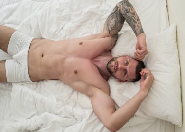 Kanepede poz veren çıplak kaslı genç adam manzarası. Yatakta yatan seksi çıplak erkek manken. Yatakta yatan çekici, çıplak bir adam. Yatakta poposu olan çıplak bir erkek manken.