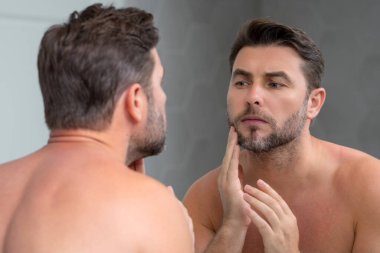 Mükemmel esmer adamın çene ve tenine dokunuşunun yakın plan portresi. Banyoda aynanın karşısında yüzüne dokunan yakışıklı bir adam. Mükemmel cilt. Erkek kozmetik, deri tedavisi. Hijyen ve cilt bakımı erkek yüzü