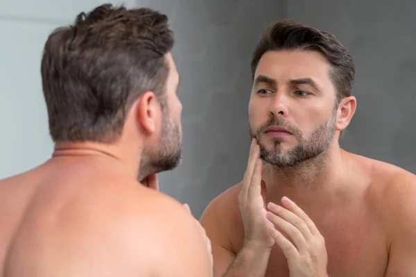 顎と肌に触れる完璧なブルネットの男のクローズアップ肖像画 風呂の中の鏡の前でハンサムな男が顔に触れている 完璧な肌だ 男性化粧品皮膚治療 衛生とスキンケア男性の顔 — ストック写真