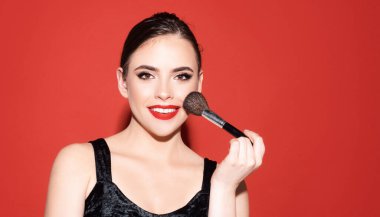 Kırmızıda doğal makyajı olan güzel bir kız modeli. Güzel esmer genç bir kadın makyaj fırçasıyla yanaklarına pudra sürüyor.