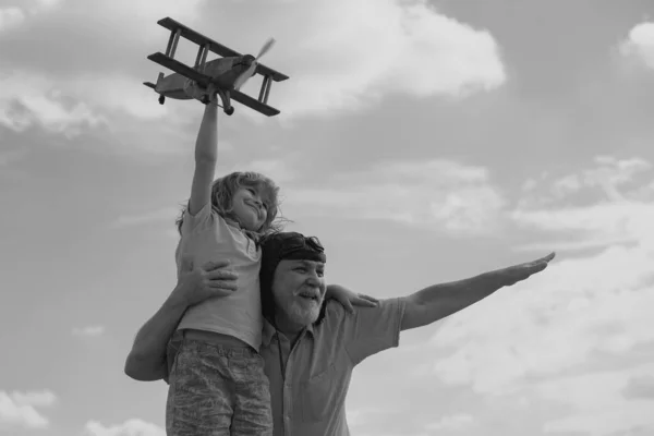 Amazed grandson child and grandfather having fun with plane outdoor on sky background with copy space. Child dreams of flying, happy childhood with grand dad
