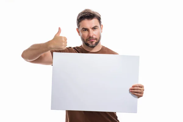 有大拇指向上的男人和空白横幅广告 在工作室的背景 男人拿着空白海报的画像 展示空白海报的男人竖起大拇指 男子展示标牌 广告牌或横幅 图库照片