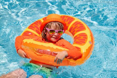 Yüzme havuzunda şişme yüzük takan çocuk. Çocuklar turuncu yüzgeçle yüzerler. Su oyuncağı, çocuklar için sağlıklı açık hava sporları. Çocuklar plaj eğlencesi
