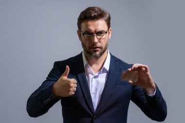Gri arka planda kredi kartı tutan bir iş adamı. İspanyol adam kredi kartını gösteriyor. Kredi kartı ya da banka kartı. İnternetten alışveriş konsepti. İndirim teklifi, online alışveriş.