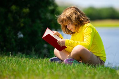 Akıllı çocuk dışarıda parkta kitap okuyor. Yazın kitap okuyan sarışın çocuk. Zeki çocuklar açık hava portresi. Çocukların hayal gücü, yenilik ve ilham kaynağı. Açık okul, öğrenen çocuklar.