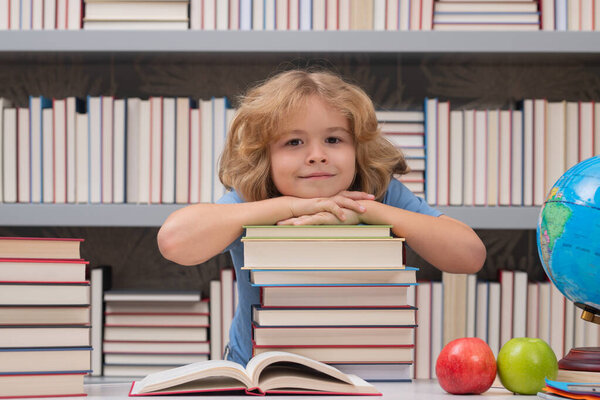 School boy with stack of books in library. Portrait of cute child school boy. School and education kids concept. Clever kid with school supplies
