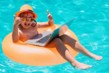 Çocuk havuzda yüzme ringinde oturuyor ve dizüstü bilgisayar kullanıyor. İnternetten alışveriş, serbest çalışma konsepti. Yaz seyahati ve iş kavramı
