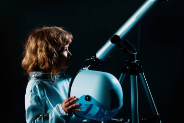 Uzay kasklı ve metal kostümlü bir astronot olmak için oynayan bir çocuk. Siyah kasklı komik çocuk portresi.