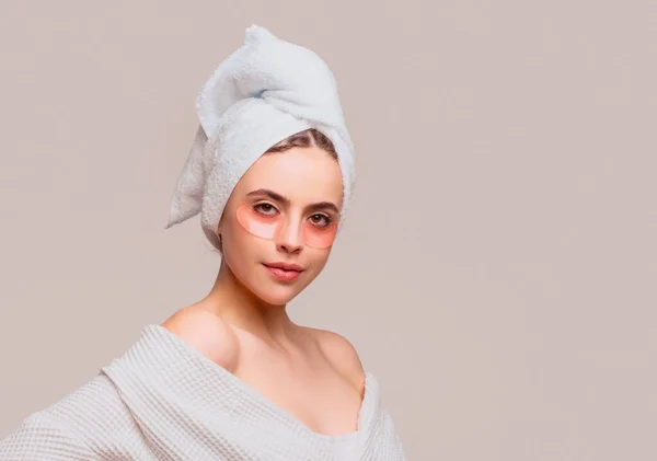 Woman applying eye patches. Close up portrait girl with towel on head. Eyes mask cosmetic patches woman face closeup. Woman applying eye patches under eyes, taking care of delicate skin around eyes
