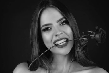 Kırmızı dudaklı ve gül çiçekli bir kadın. Ağızda gül çiçekleri. Stüdyo arka planında moda güzellik portresi. Kırmızı gül tutan baştan çıkarıcı bir kadın. Dişleri siyah, izole bir arka plan.