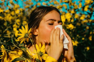 Portrait of an allergic woman surrounded by seasonal flowers wearing bright yellow sweater. Charming girl is blowing her nose near autumn yellow flowers in bloom clipart