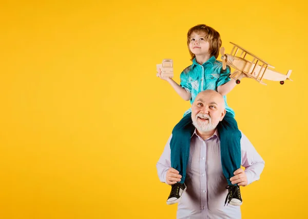 Grandfather and son piggyback ride with plane and wooden toy truck. Men generation granddad and grandchild. Elderly old relative with child