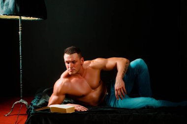 Seksi yakışıklı genç adam yatakta üstsüz yatıyor, kitap okuyor. Yakışıklı bir entelektüel.