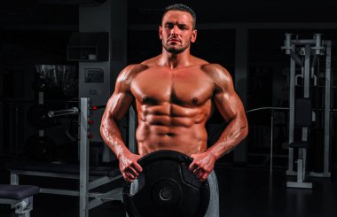 Spor salonunda ağırlık diski olan bir Powerlifter. Vücut geliştirici pazılarını eğitiyor.