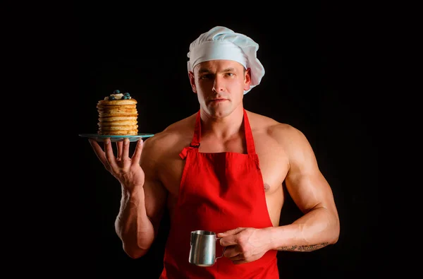 Sexy muscular man in chefs hat with sweet homemade stack of pancakes with syrup. Chef muscle man with apron bake pancakes with berries and maple syrup