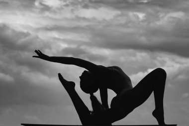 Genç, formda bir kadının silueti esniyor. Sportif genç kız spor yapıyor, sağlıklı bir hayat sürüyor. Bulutlu gökyüzü arkaplanı