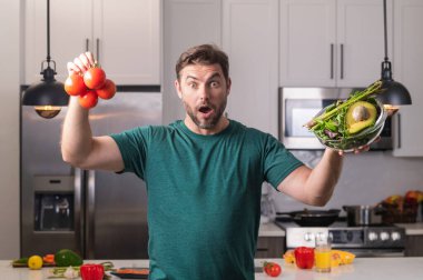 Mutfakta yemek yapan orta yaşlı bir adam. Mutfakta sebzeli adam. Mutfakta sebze malzemeleriyle yemek pişiren sıradan bir adamın portresi. Adam mutfakta salata hazırlıyor.