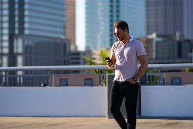 Sınıf polo tişörtlü genç yakışıklı sokakta telefonla sohbet ediyor. Yakışıklı, kendine güvenen hippi model dışarıda telefonla konuşuyor. İş telefonu görüşmesi