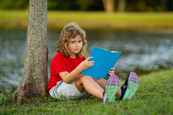 Smart clever Kids. Cute child read books outdoors. Kids learning and summer education. Child boy reading book outdoor on green grass field. Child is learning and reading. Kid read book in the garden