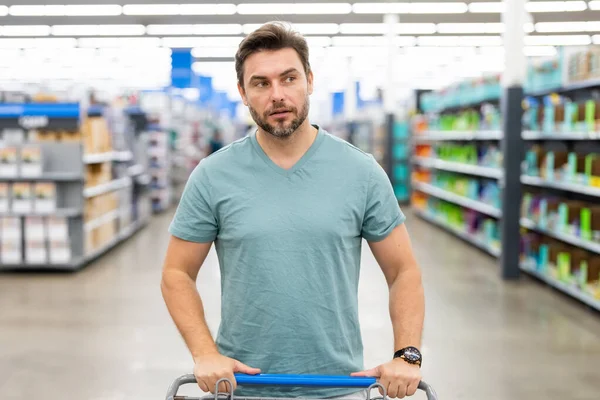 Portrait of man with shopping cart in a store. Supermarket shopping and grocery shop concept. Shopping. Guy buying grocery in supermarket hold shopping basket