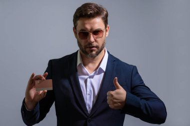 Ciddi kibirli bir iş adamının gri arka planda plastik kredi kartı gösteren portresi. İş ve başarı kavramı. İnternetten alışveriş. Çevrimiçi ödeme. Kredi kartının bakiyesi