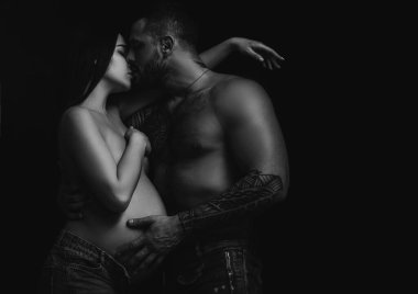 Dövmeli erkek arkadaşın hamile kız arkadaşına sarılıp öpüyor. Gerçekten romantik ve tutkulu bir an. Dövmeli sakallı adam, güzel kız arkadaşını kapıyor. Seksi çiftin duyguları