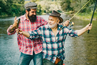 İki erkek arkadaş balık tutuyor. Balıkçı oltası, nehir suyunda durarak oyuncu seçiyor. Yaşlı ve genç balıkçı. Mutlu heyecanlı erkek arkadaşlar