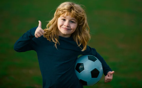 stock image Young soccer player in sportswear with soccer ball show thumbs up success sign. Cheerful little boy enjoy soccer, football sport games. Boy holding soccer ball, close up sporty kids portrait