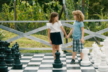 Büyük satranç tahtasında oynayan sevimli küçük çocuklar. İki mutlu gencin portresi yaz parkında satranç oynuyor.