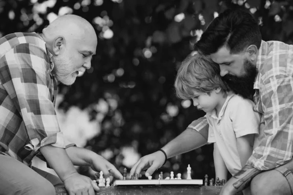 家族の休日と一体感 父と祖父と一緒に公園で一緒に楽しむ少年 男性多世代家族 チェスをする子供 — ストック写真