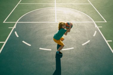 Oyun sahasında basketbol oynayan küçük bir çocuğun üzerinden açılı görüş.