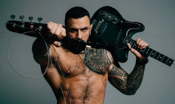 Guitarist breaks guitar. Excited sexy man with electric guitar. Macho with muscular torso with crash electric guitar