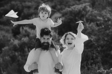 Baba anne ve oğlu parkta. Baba anne ve oğlu eğleniyor ve doğada oynuyorlar. Mutlu sevgi dolu bir aile. Ebeveynler ve çocuk. Güneşli bir günde basit kağıt uçaklarla oynayan çocuklar