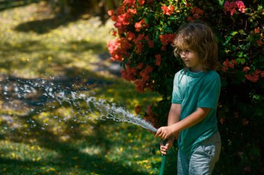 Yaz günü bahçede çiçekleri sulayan sevimli küçük bir çocuk. Çocuk bahçe hortumu kullanıyor. Bahçede çiçek sulayan komik çocuk.