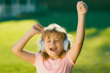Şarkı söyleyip dans eden çocuklar. Mutlu çocuk yeşil çimen arka planında kulaklıkla müzik dinlemeyi seviyor. Kulaklıklı komik çocuk yaz parkında ya da arka bahçede müzik dinliyor.