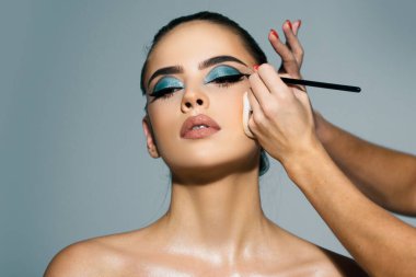 Makyöz göz farı sürüyor. Vizeci bir el, genç bir güzellik modelinin kozmetik ürünlerini boyuyor. Parlak makyajlı güzel bir genç kızın portresi.