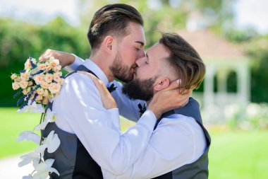 Evli LGBT çiftleri romantik bir düğün törenini bir buket çiçekle kutluyorlar. Düğünde eşcinsel öpücüğü. Evli eşcinsel çift öpüşüyor. Gey öpücüğünün yakın portresi