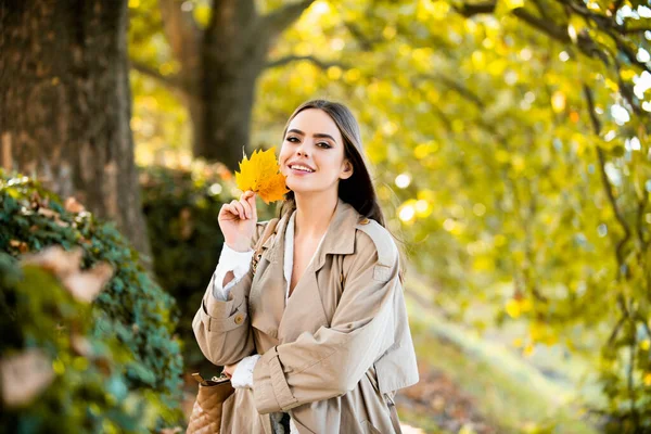 在秋天的大自然里 快乐的女人把秋天的叶子挂在脸上 长满秋天枫叶的年轻女子的画像 漂亮的姑娘在公园里散步玩落叶游戏 温暖的秋天秋季时装 — 图库照片